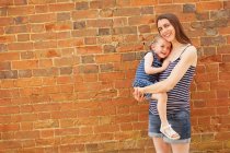 Portrait of pregnant mid adult woman carrying daughter by brick wall — Stock Photo