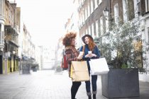 Two young women holding shopping bags and coffee cup on street — Stock Photo