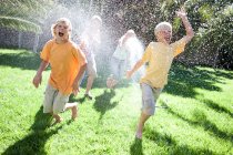 Eltern im Garten besprühen Söhne mit Wasser aus Schlauchleitung — Stockfoto