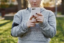 Молода жінка тренується в парку і дивиться на смартфон — стокове фото
