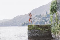 Young male standing on pier with arms open, Lake Como, Lombardy, Italy — Stock Photo