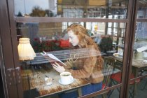 Vista através da janela da mulher na leitura da cafetaria — Fotografia de Stock