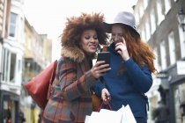 Дві молоді жінки дивляться на смартфон і сміються — стокове фото