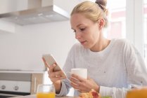 Jeune femme regardant smartphone à la table du petit déjeuner — Photo de stock