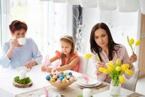 Femme avec fille et mère arrangeant des tulipes jaunes à la table à manger de Pâques — Photo de stock