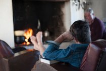 Über-die-Schulter-Blick von Senior und Sohn zu Hause vor Holzfeuer — Stockfoto