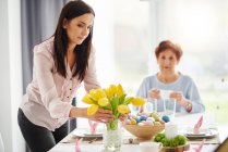 Взрослая женщина устраивает желтые тюльпаны за пасхальным столом — стоковое фото