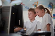 Schoolboy and girl using computer in classroom at primary school — Stock Photo