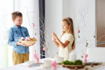 Niña y hermano decorando ramitas con coloridos huevos de Pascua - foto de stock