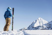 Vista trasera del esquiador de pie en la nieve y mirando a las montañas - foto de stock