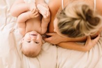 Overhead portrait of cute baby girl lying on bed with mother — Stock Photo