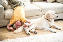 Мальчик лежит вверх ногами на диване с собакой — стоковое фото