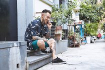 Young man sitting on doorstep in residential alleyway making smartphone call, Shanghai French Concession, Shanghai, China — Stock Photo