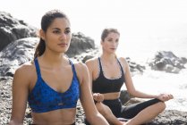 Zwei junge Frauen praktizieren Yoga am Strand — Stockfoto
