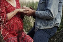 Sección media de pareja embarazada romántica cogida de la mano - foto de stock