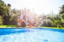 Father and sons in mid air jumping into outdoor swimming pool — Stock Photo