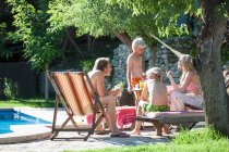 Família relaxante por piscina exterior — Fotografia de Stock