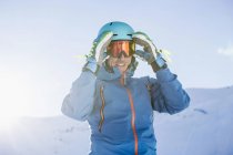 Portrait of skier on mountain adjusting goggles — Stock Photo