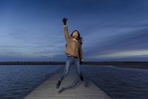 Young woman jumping on pier at dusk — Stock Photo