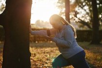 Изогнутая молодая женщина тренируется в парке со смартфоном — стоковое фото