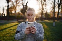 Молода жінка тренується в парку і дивиться на смартфон — стокове фото