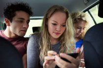Друзі на задньому сидінні автомобіля дивляться на смартфон — стокове фото