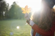 Frau hält Herbstblatt im Sonnenlicht — Stockfoto