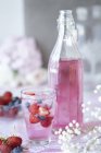 Glass of berry cordial with fresh fruit, bottle of cordial beside glass, close-up — Stock Photo