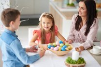 Girl with brother and mother preparing colourful easter eggs at dining table — Stock Photo