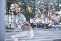 Jovem hipster masculino no assento da janela do café segurando smartphone, Shanghai French Concession, Shanghai, China — Fotografia de Stock