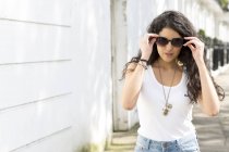 Jovem mulher passeando na rua e colocando óculos de sol — Fotografia de Stock