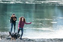 Две молодые женщины бегают с собакой у реки — стоковое фото