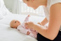 Young woman dressing baby daughter on bed — Stock Photo