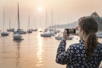 Vista trasera de la mujer fotografiando barcos al atardecer, Lazise, Veneto, Italia, Europa - foto de stock