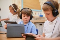 Escolares e meninas ouvindo fones de ouvido na sala de aula na escola primária — Fotografia de Stock