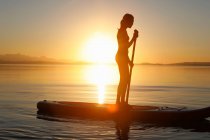 Молода дівчина весло на воді, на заході сонця — стокове фото