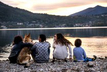 Veduta posteriore del ragazzo con la famiglia e il cane sul fiume al tramonto, Vercurago, Lombardia, Italia — Foto stock