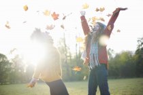 Amigos femininos jogando folhas de outono no ar — Fotografia de Stock