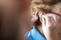 Mujer madura ayudando a la mujer mayor a insertar audífonos, primer plano, enfoque diferencial - foto de stock