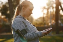 Изогнутая молодая женщина тренируется в парке и смотрит на смартфон — стоковое фото