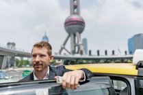 Young businessman beside yellow cab at Shanghai financial center, China — Stock Photo