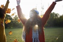 Two young women throwing autumn leaves in air — Stock Photo