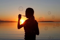 Young girl, outdoors, blowing bubbles, at sunset — Stock Photo