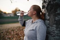 Викривлена молода жінка тренує і п'є пляшкову воду в парку — стокове фото