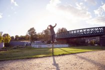 Frau balanciert auf Pfosten am Kanal, Brücke im Hintergrund — Stockfoto