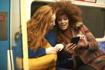 Two young women looking at smartphone in train — Stock Photo