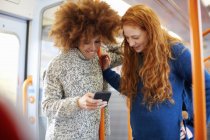 Friends looking at on mobile phone in train — Stock Photo