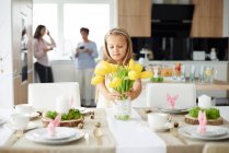 Girl arranging yellow tulips at easter dining table — Stock Photo