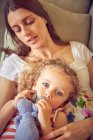 Pregnant woman and daughter reclining on sofa with soft toy — Stock Photo