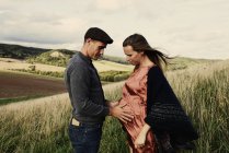 Romantic man with hands on pregnant wife stomach on hillside — Stock Photo